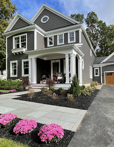 Gray 2-story house with white trim and pink mums bordering sidewalk